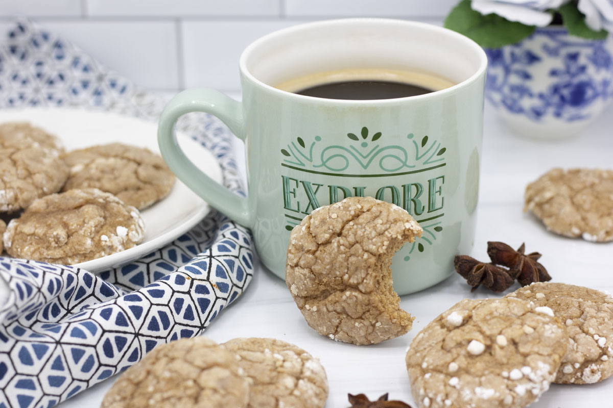 Spice cake crinkle cookies scattered around and one cookie with a bite propped against a mug