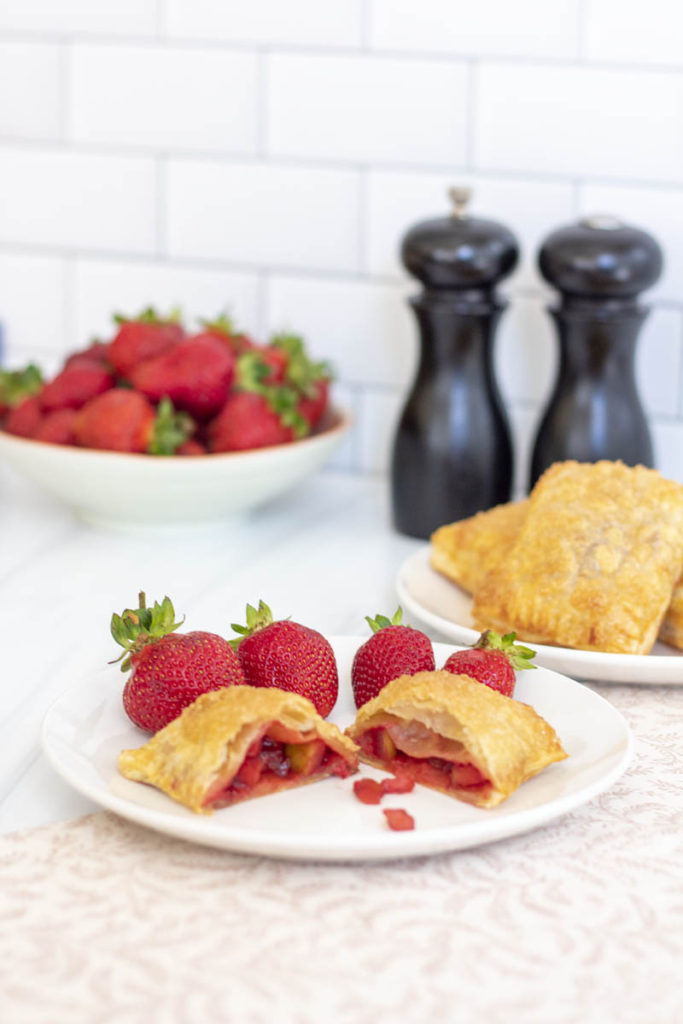 A cut strawberry apple hand pie with freshly baked hand pies around