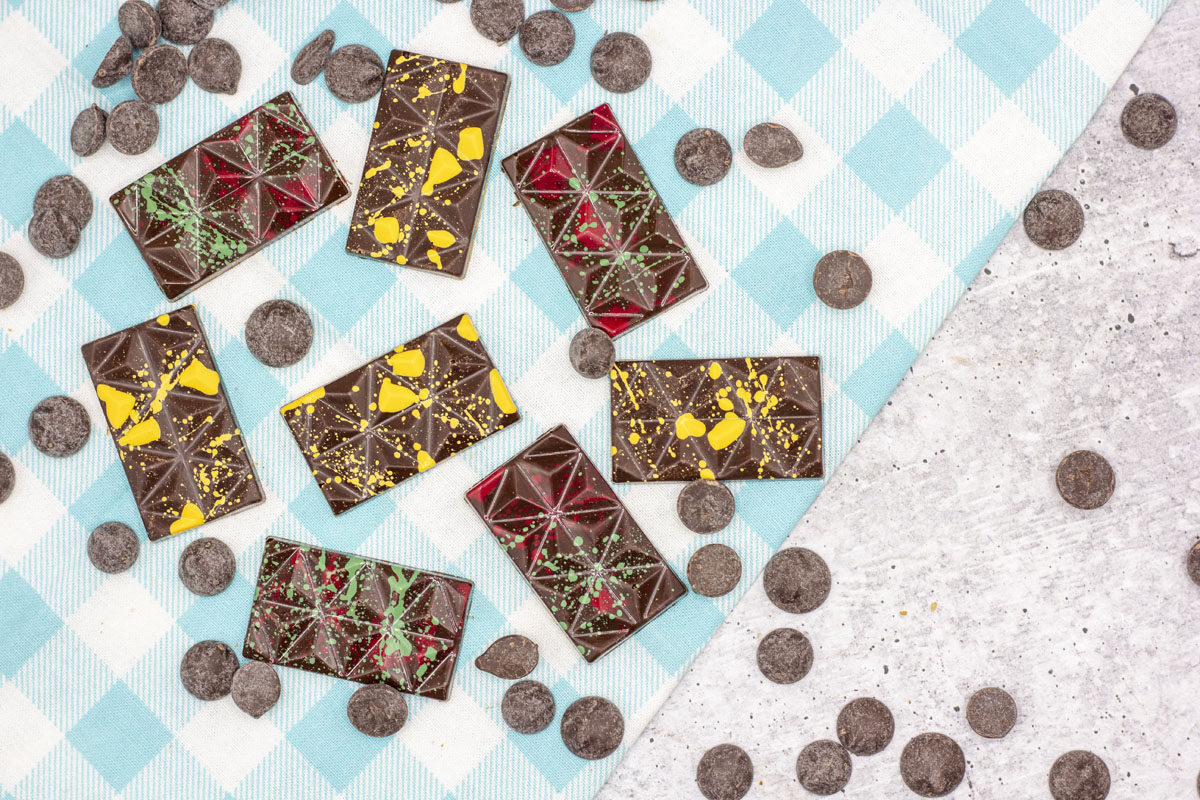 Cocoa butter colors splattered on tempered chocolate in tiny bars amidst chocolate callets