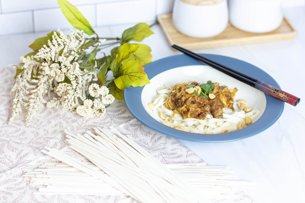 slow cooker thai peanut chicken over rice noodles with chopsticks on the bowl