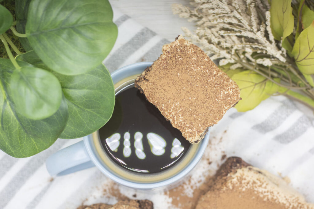 Tiramisu brownie square perched on the lip of a coffee mug