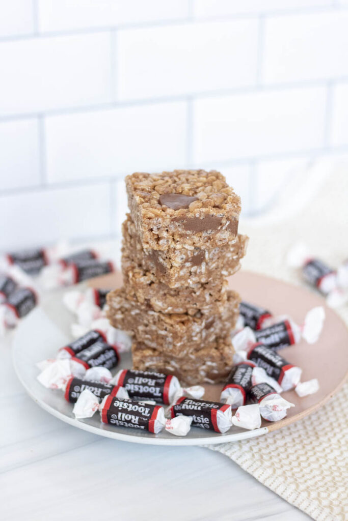 Tootsie roll rice krispies stacked up tall on a plate of miniature tootsie rolls
