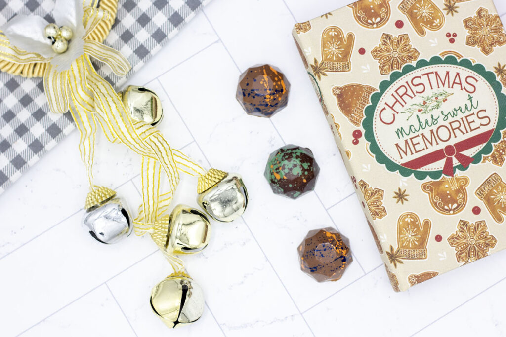 Cocoa butter splattered truffles alongside bells and a small Christmas book